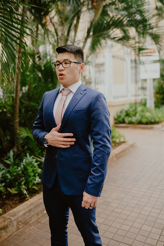 A groom stands in his dark blue suit with a pink tie and white shirt. He has his hand over his chest while taking a deep breath moments before his first glimpse of his bride at their Cafe Julia  wedding