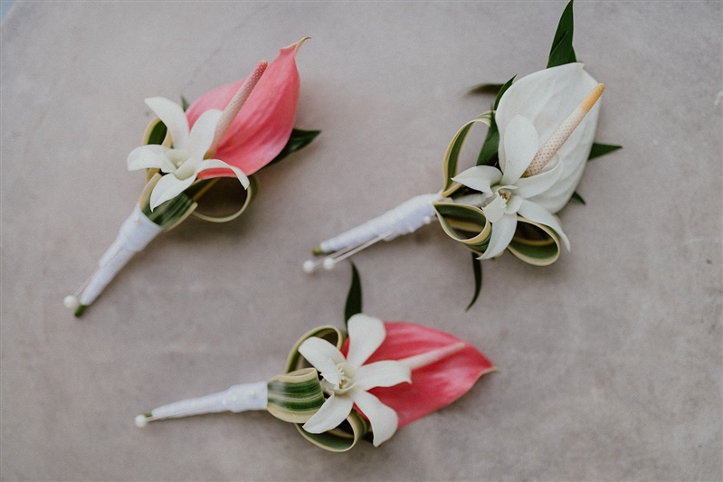 Three boutonnieres for a wedding. All three feature calla Lilys, two pink and one white.