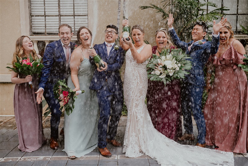 A bride and groom open and spray a bottles of champaign while their groomsmen and bridesmaids celebrate at their Cafe Julia wedding