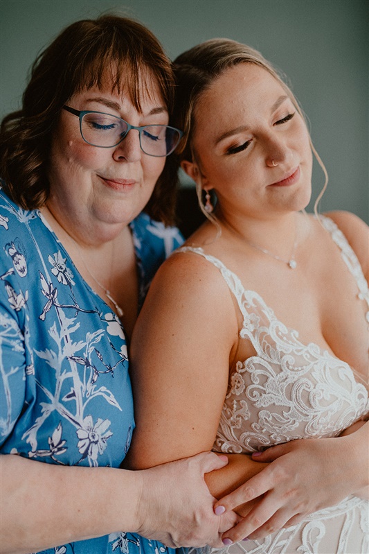 A bride in her wedding dress cuddles up to her m other as they hold hands before their wedding.