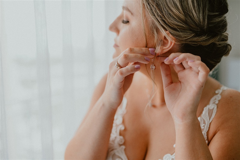 A closeup of a blonde bride putting on her earrings