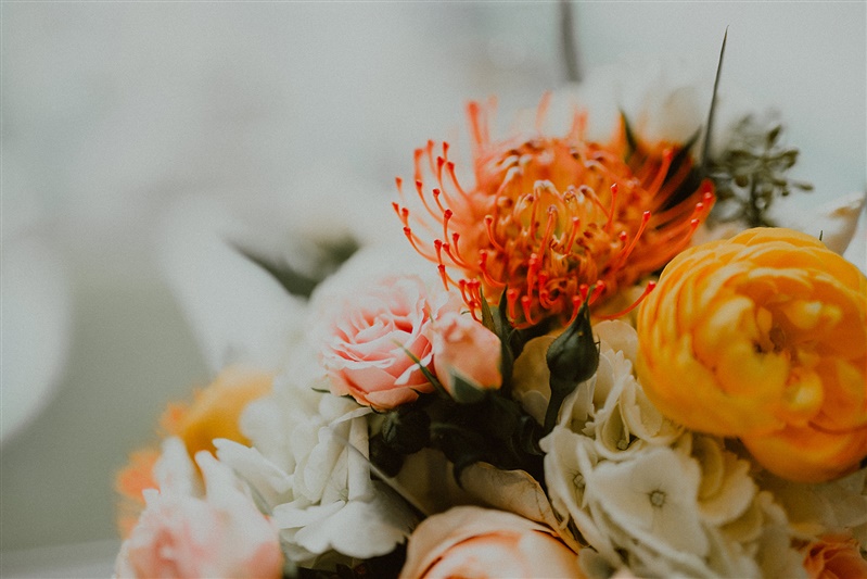 an up close photo of a wedding bouquet. The flowers are various shades of orange, white, and light pink.