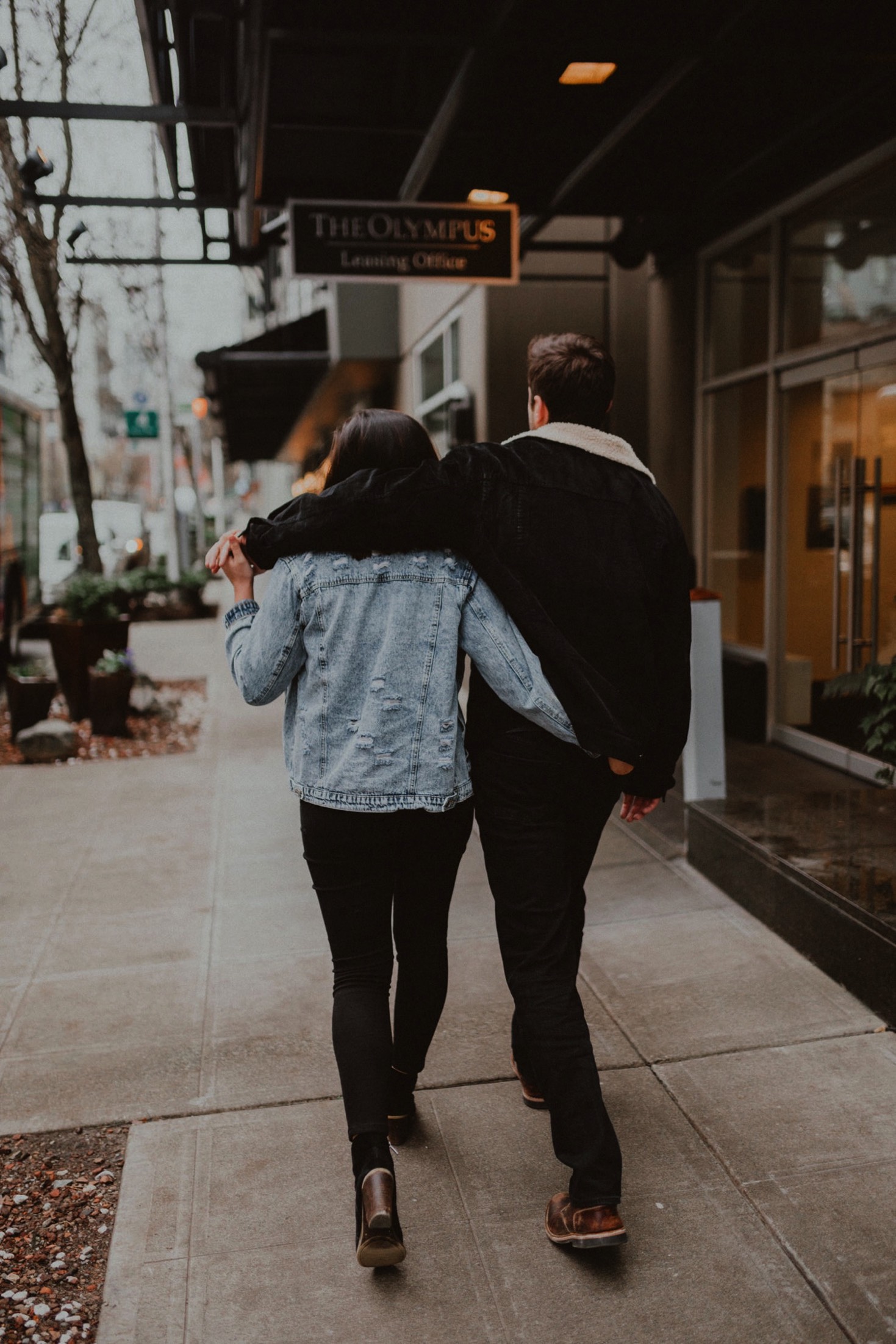 A man and woman wearing denim jackets wrap their arms around each other as they walk through Seattle.