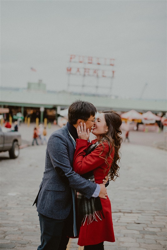 A man and woman kiss in front of the Pike Place Market sign for their Seattle engagement photos with Chelsea Abril.