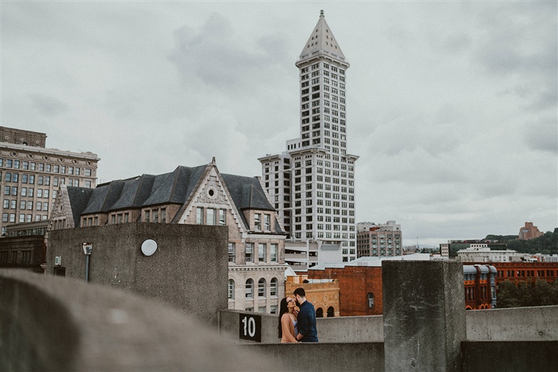 A candid shot of a couple kissing on top of the Seattle Public Library with the city in the background