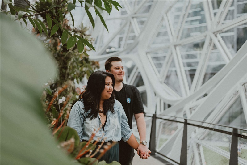 An engaged couple hold hands while walking through the Seattle Spheres with engagement photographer Chelsea Abril.