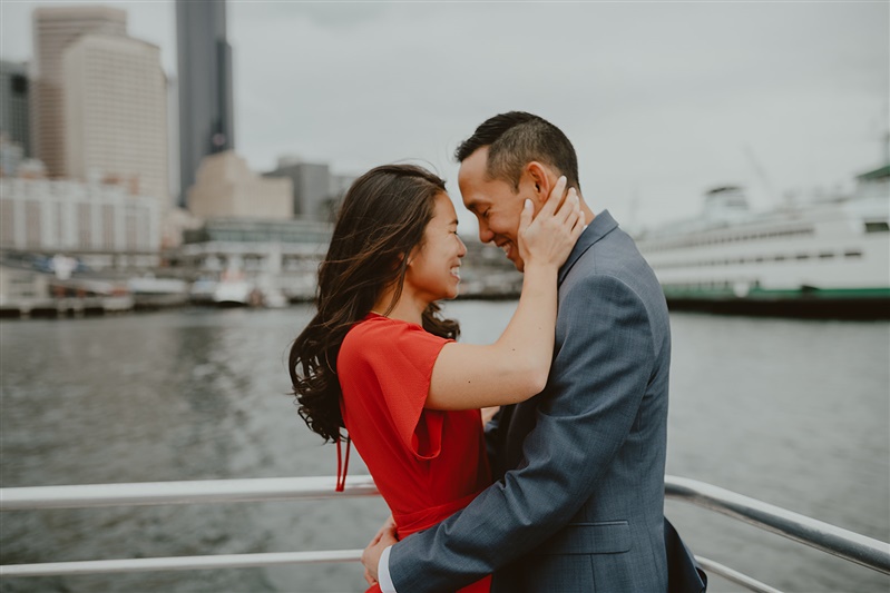 A smiling engaged couple pose at the Alki Water Taxi Docks for engagement pictures with Seattle engagement photographer Chelsea Abril