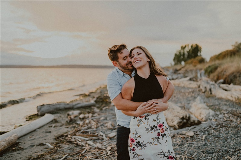 A man wraps his arms around his fiance at the Seattle waterfront in Discovery Park during their engagement photo session.