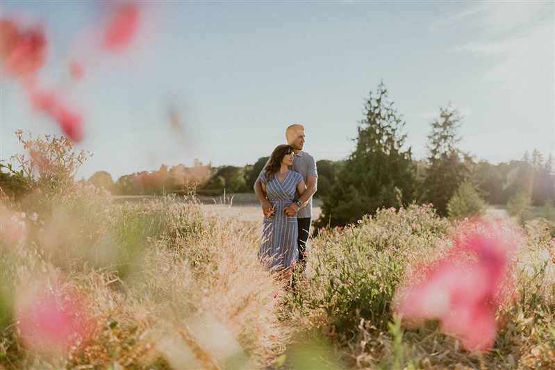 A man holds his arms around his fiance as they have their engagement photos taken by Chelsea Abril photography in Discovery Park, Seattle.