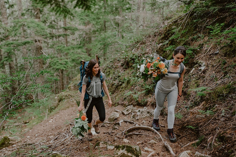 Two women holding flower bouquets hike together Granite Falls near Seattle, Washington.