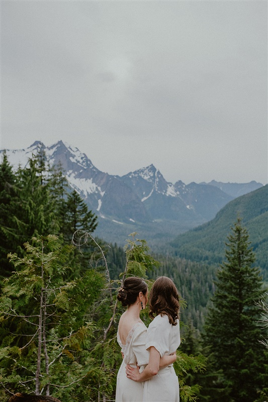 Two brides stand together while eloping on a mountain in Granite Falls near Seattle.