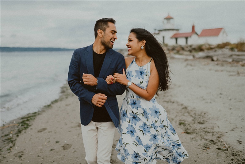 A man and his fiance walk along the beach in front of a lighthouse in Seattle.