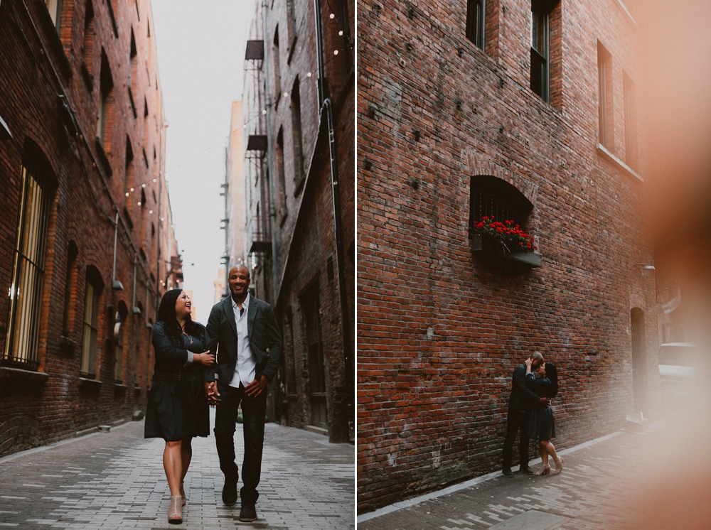 A woman in a black dress holds hands with her fiance in a black suit as they walk the streets of downtown Seattle.