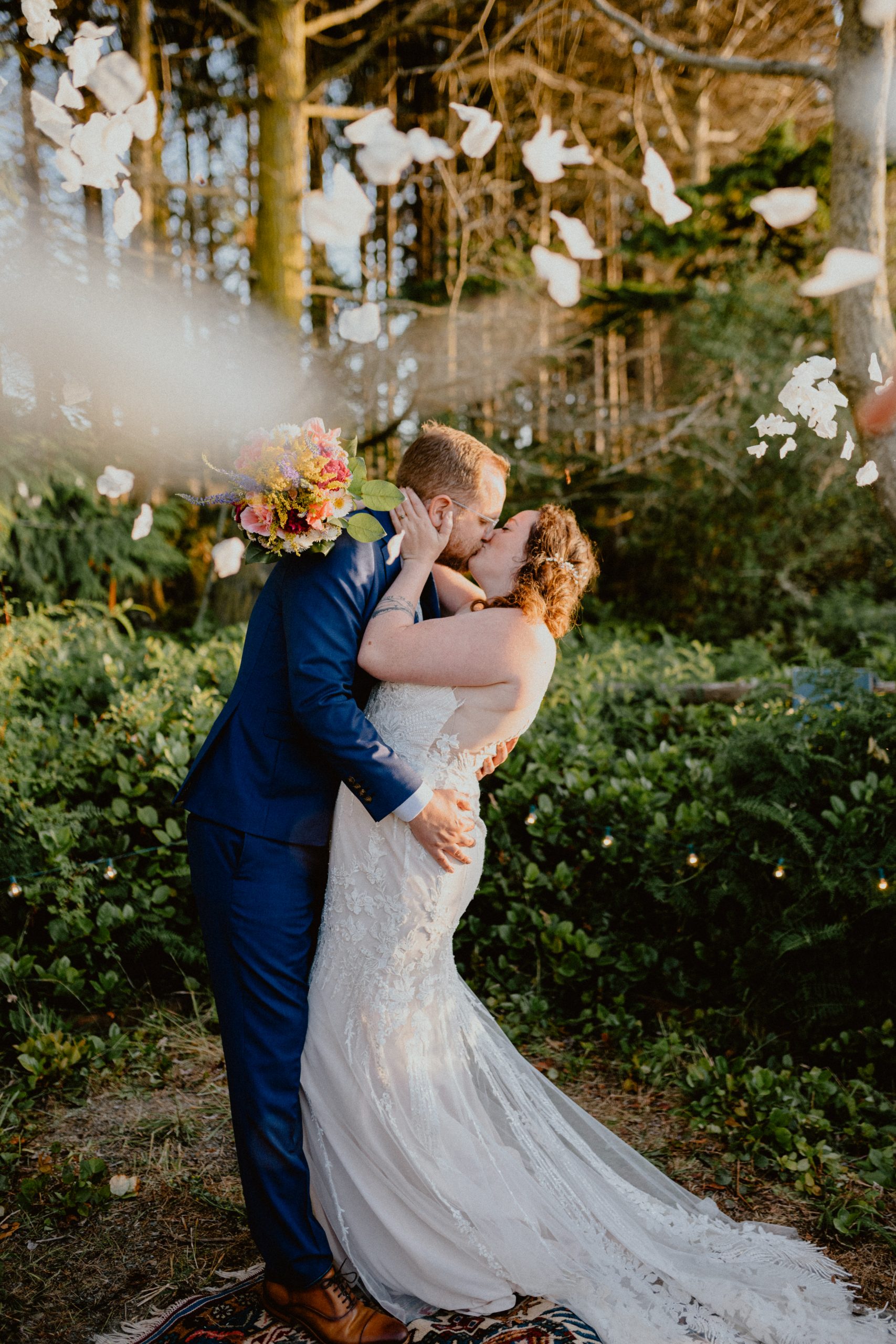 Bride and Groom embrace in a kiss with flower petals falling around them in an outdoor wedding ceremony | Washington State Elopement Photographer, Seattle Elopement Photographer, Newlywed Elopement Photographer, Quarantine Wedding Elopement Inspiration | chelseaabril.com