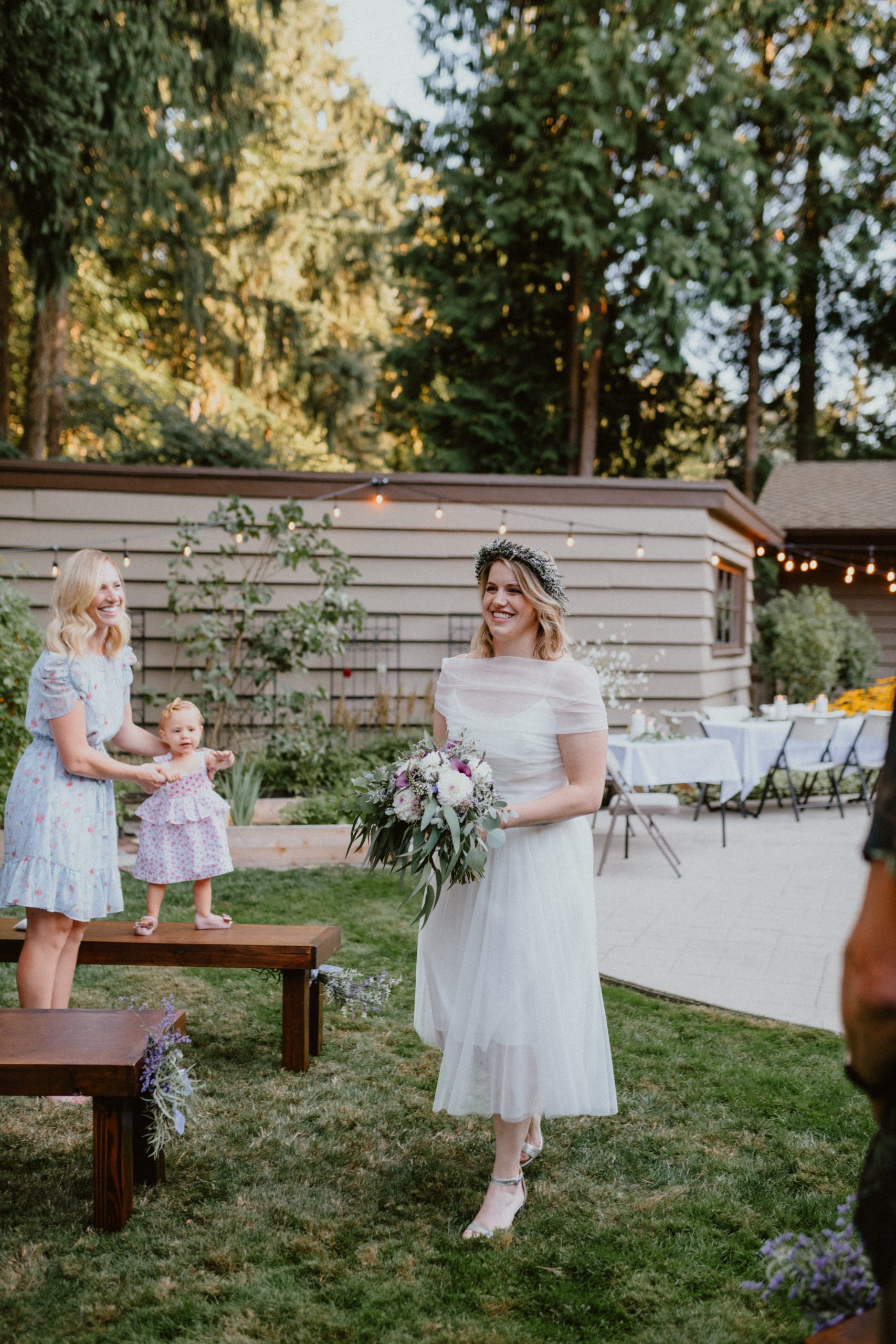 Bride walks down the aisle surrounded by family smiling at her, she wears a short wedding dress and lavender flower crown | Seattle Wedding Photographer, Seattle Elopement Photographer | chelseaabril.com