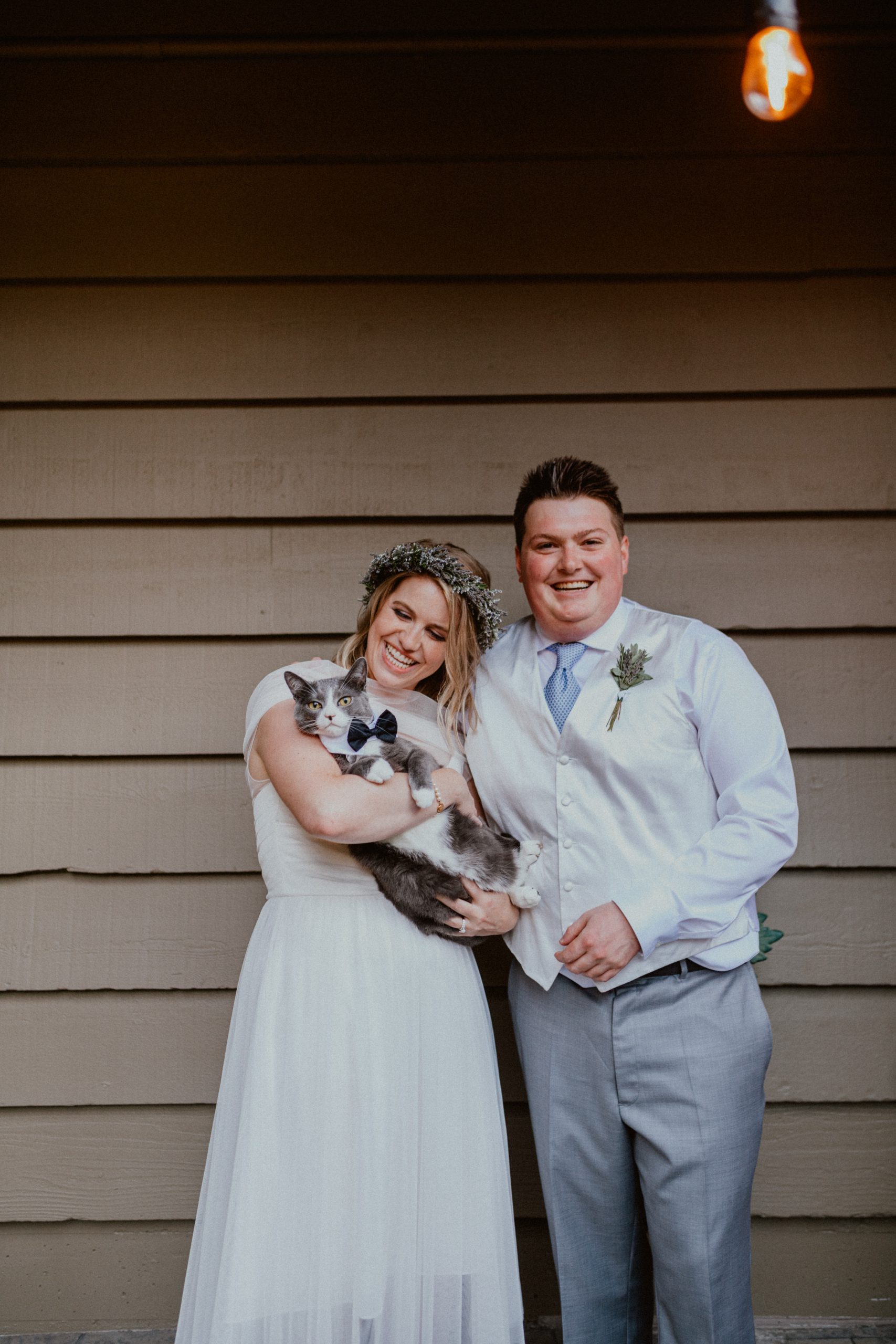 Bride and groom laugh and hold their cat wearing a bowtie after backyard wedding ceremony | Seattle Wedding Photographer, Seattle Elopement Photographer | chelseaabril.com