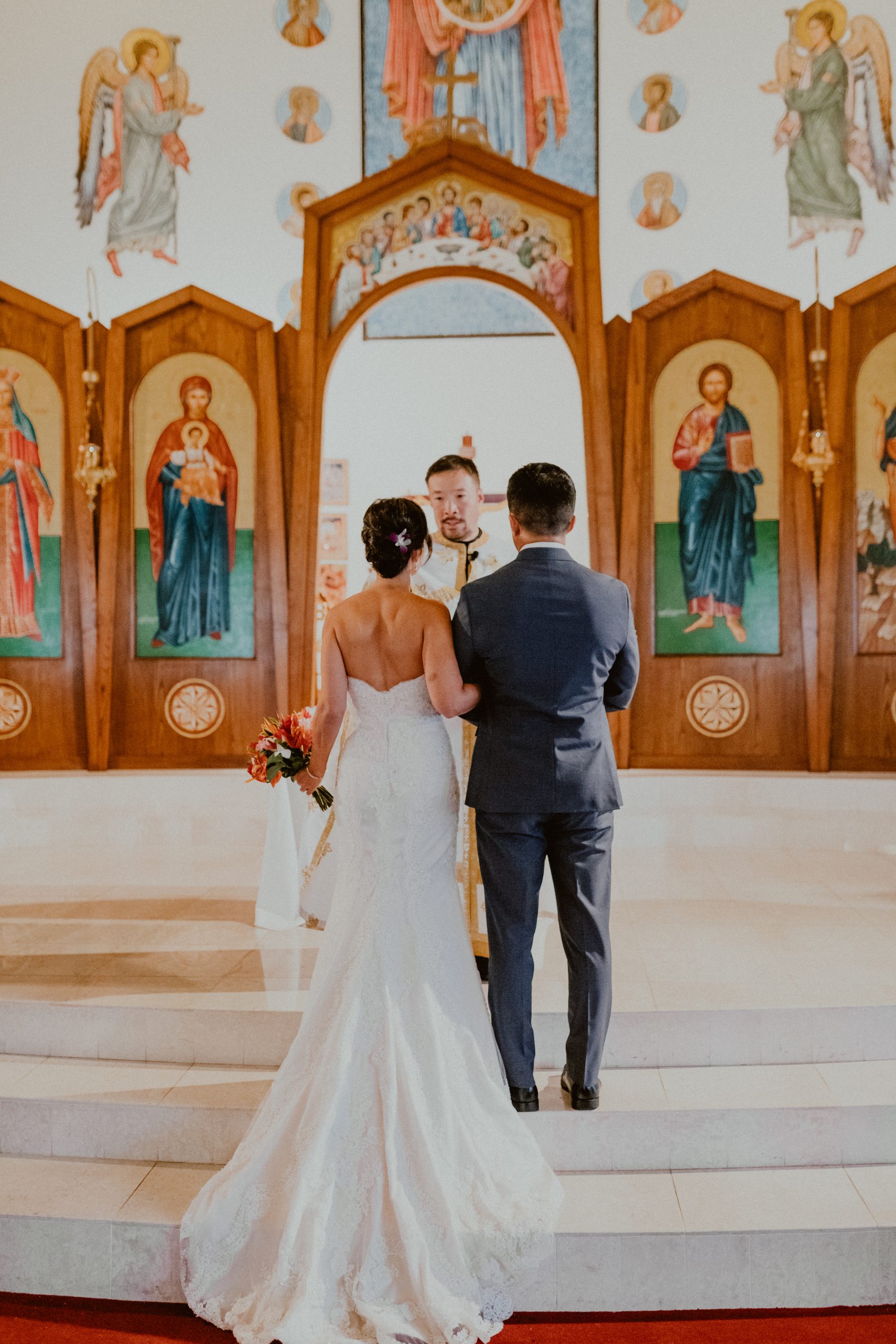 Bride and groom stand at the altar with their backs to the Hawaii wedding photographer and facing the priest while they say their vows