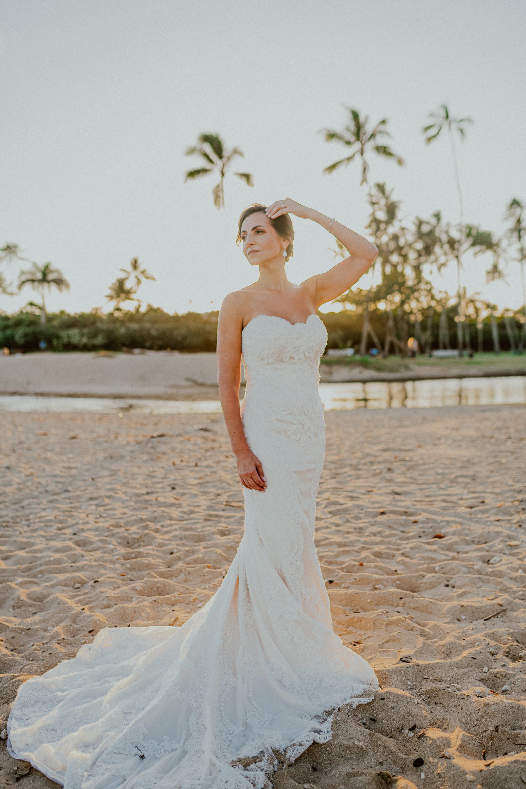 Bride models her white lace strapless style wedding dress at sunset on the Oahu beach after her traditional Hawaiian church ceremony | Oahu Wedding Photographer, Oahu Elopement Photographer, Destination Wedding Photographer, Destination Elopement Photographer, Newlywed moments ideas, Newlywed Photography inspiration, Hawaii Elopement ideas | chelseaabril.com