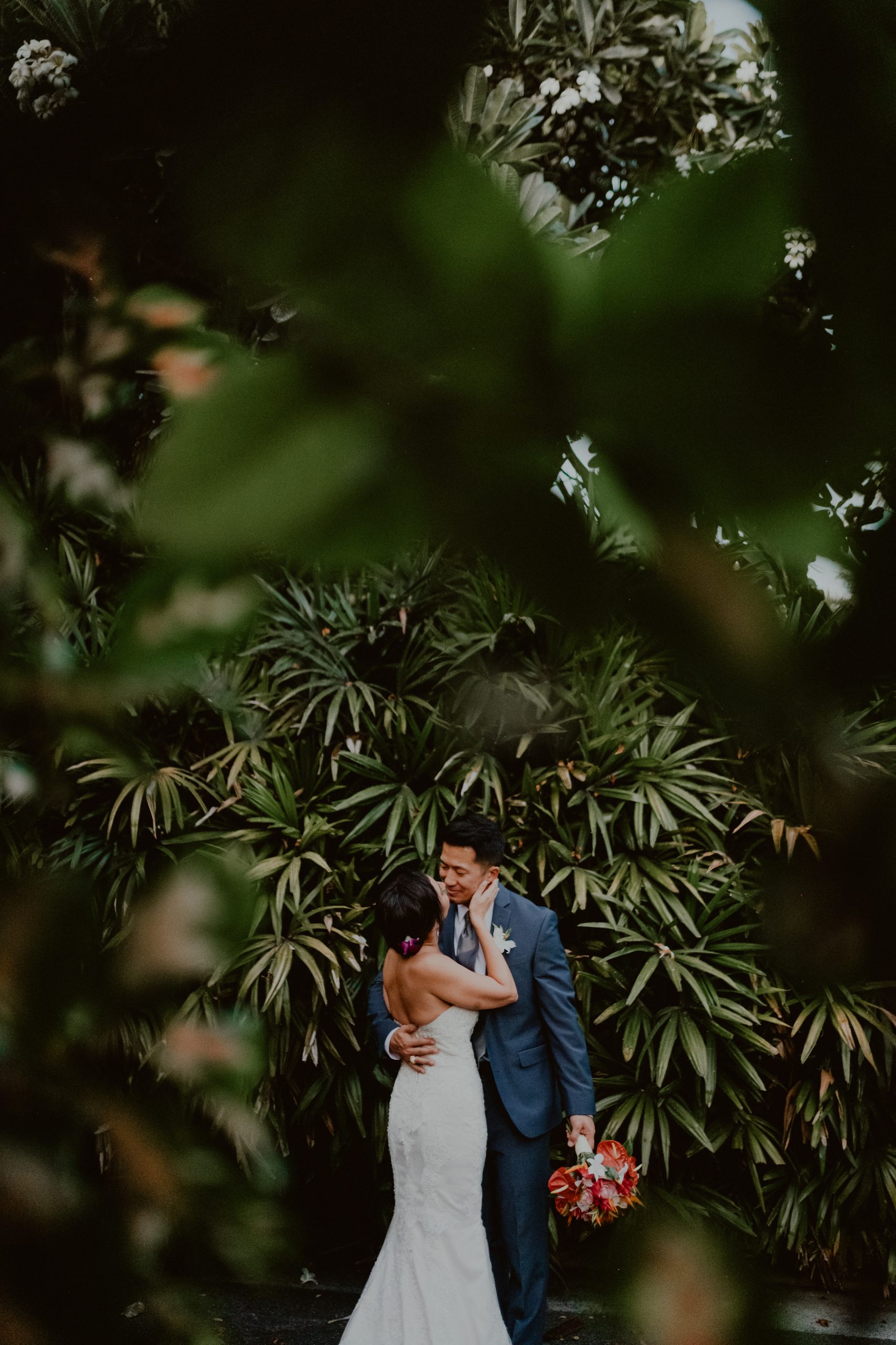 Bride and groom kiss each other on the long road surrounded by Palm leaves and native Hawaiian plants and foliage,