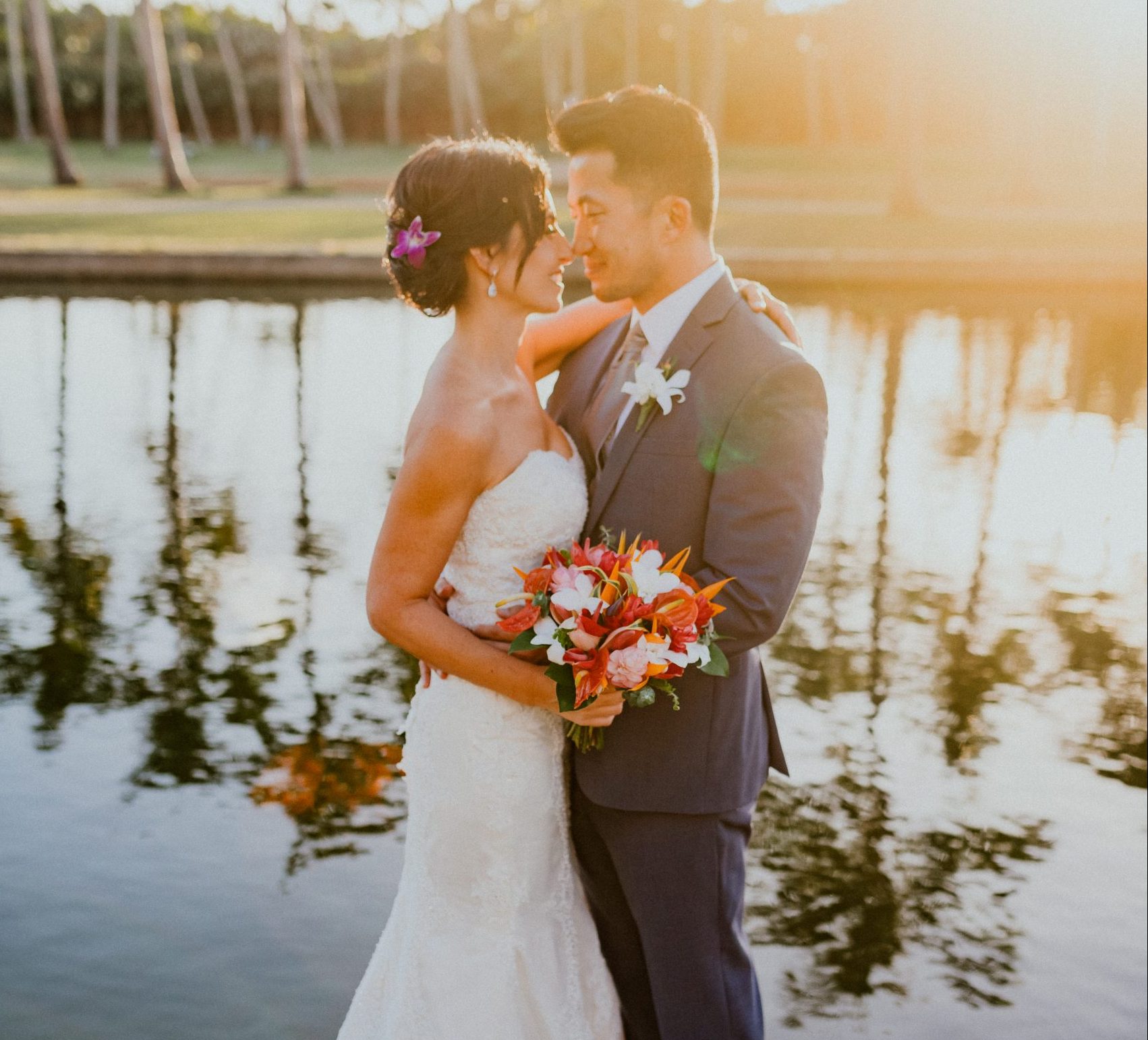 Bride and Groom kiss in front of reflection pool at sunset on Oahu Hawaii. Bride holds her wedding bouquet dressed in a strapless wedding dress with a train and wearing a updo bridal style | Oahu Wedding Photographer, Oahu Elopement Photographer, Destination Wedding Photographer, Destination Elopement Photographer, Newlywed moments ideas, Newlywed Photography inspiration, Hawaii Elopement ideas | chelseaabril.com