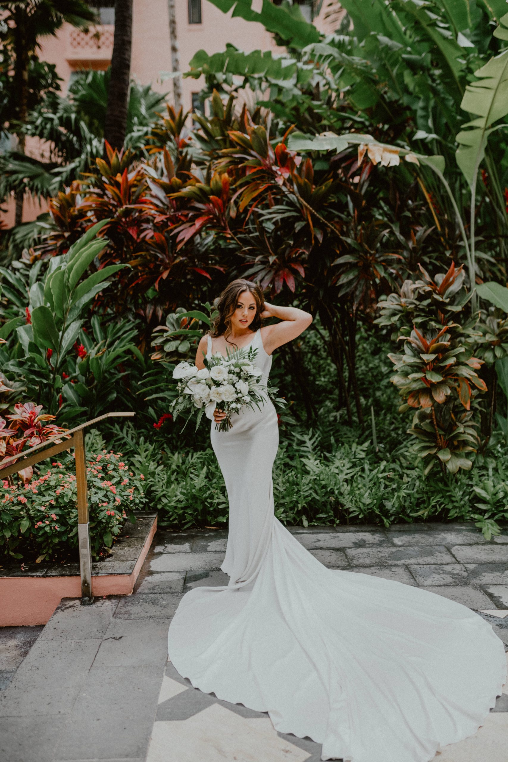 Bride walks down the hotel stairs while carrying white bouquet of flowers with her white silk wedding dress with a long dress and a half up half down bridal hairstyle | Oahu Wedding Photographer, Oahu Elopement Photographer, Destination Wedding Photographer, Destination Elopement Photographer, Newlywed moments ideas, Newlywed Photography inspiration, Hawaii Elopement ideas | chelseaabril.com