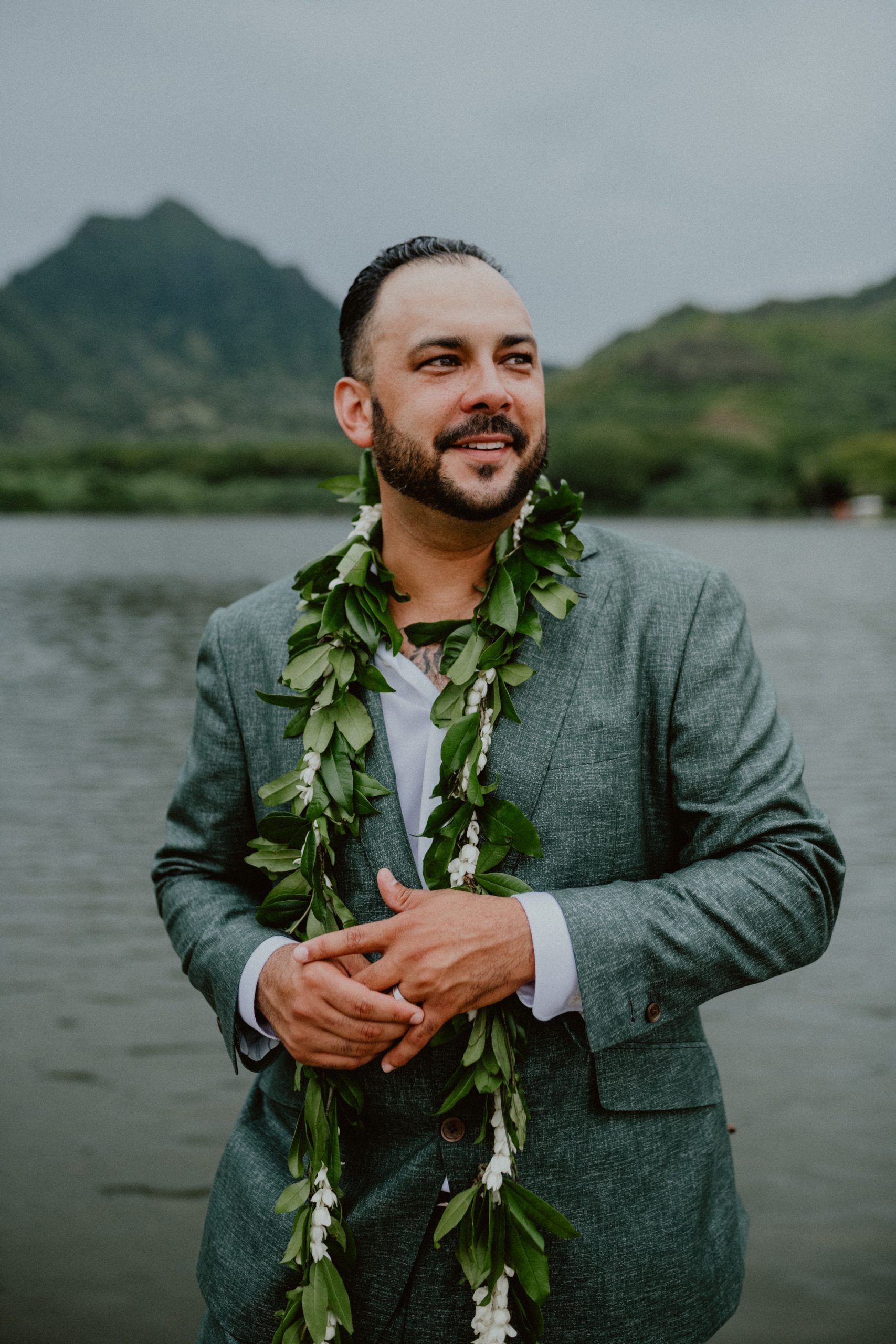 Groom stands in front of the water at the beach of Kualoa Ranch while wearing a traditional lei after the Oahu wedding ceremony | Oahu Wedding Photographer, Oahu Elopement Photographer, Destination Wedding Photographer, Destination Elopement Photographer, Newlywed moments ideas, Newlywed Photography inspiration, Hawaii Elopement ideas | chelseaabril.com