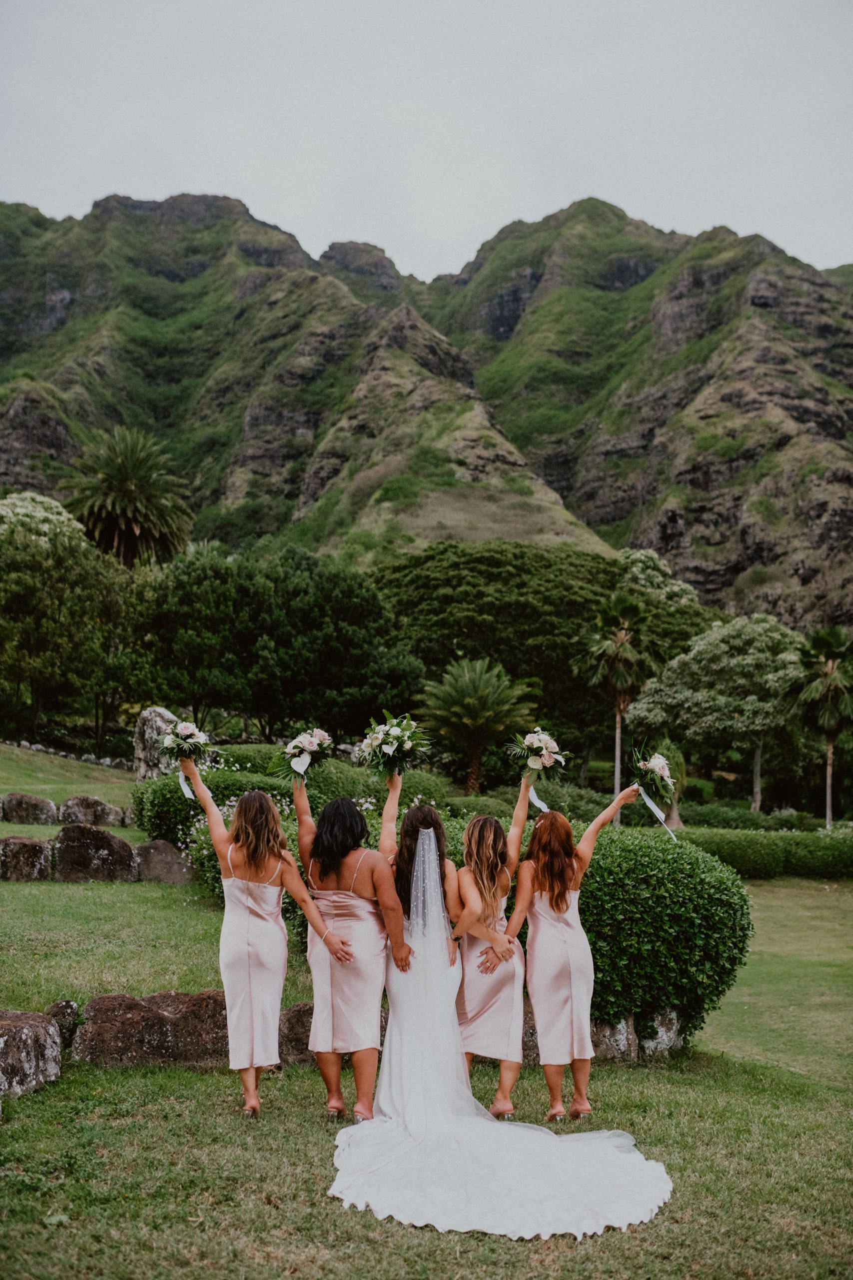 Bride and Bridesmaids hold up their wedding bouquets at the Kualoa Ranch Wedding in front of the Oahu Mountains on the Islands | Oahu Wedding Photographer, Oahu Elopement Photographer, Destination Wedding Photographer, Destination Elopement Photographer, Newlywed moments ideas, Newlywed Photography inspiration, Hawaii Elopement ideas | chelseaabril.com