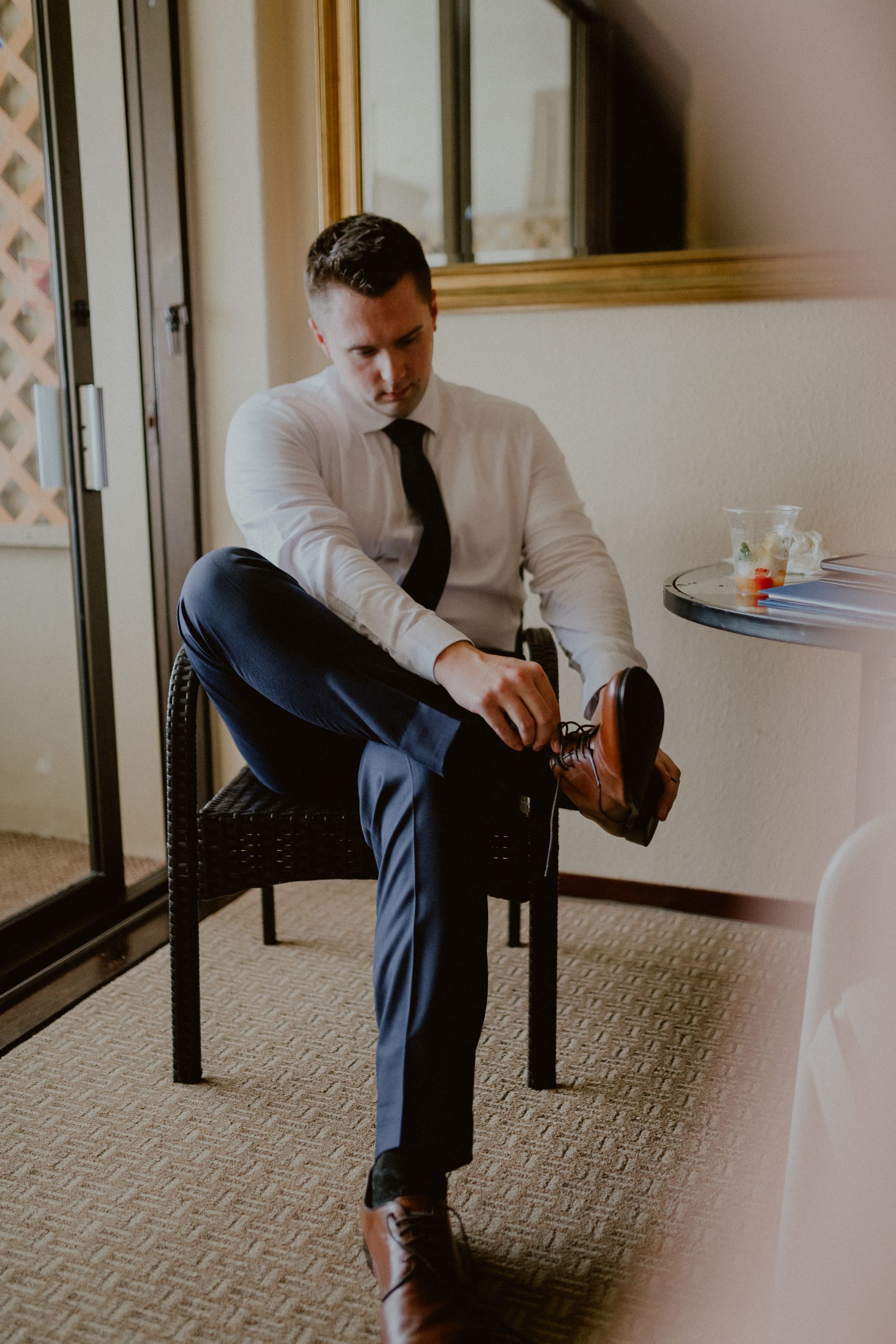 Groom gets ready for his wedding ceremony while putting on a tan dress shoe, while wearing a dark blue suit and getting ready in his hotel room | Groom style tips, Groom wedding day inspiration, Groom Tips Wedding, Groom tips for men, Groom tips | chelseaabril.com