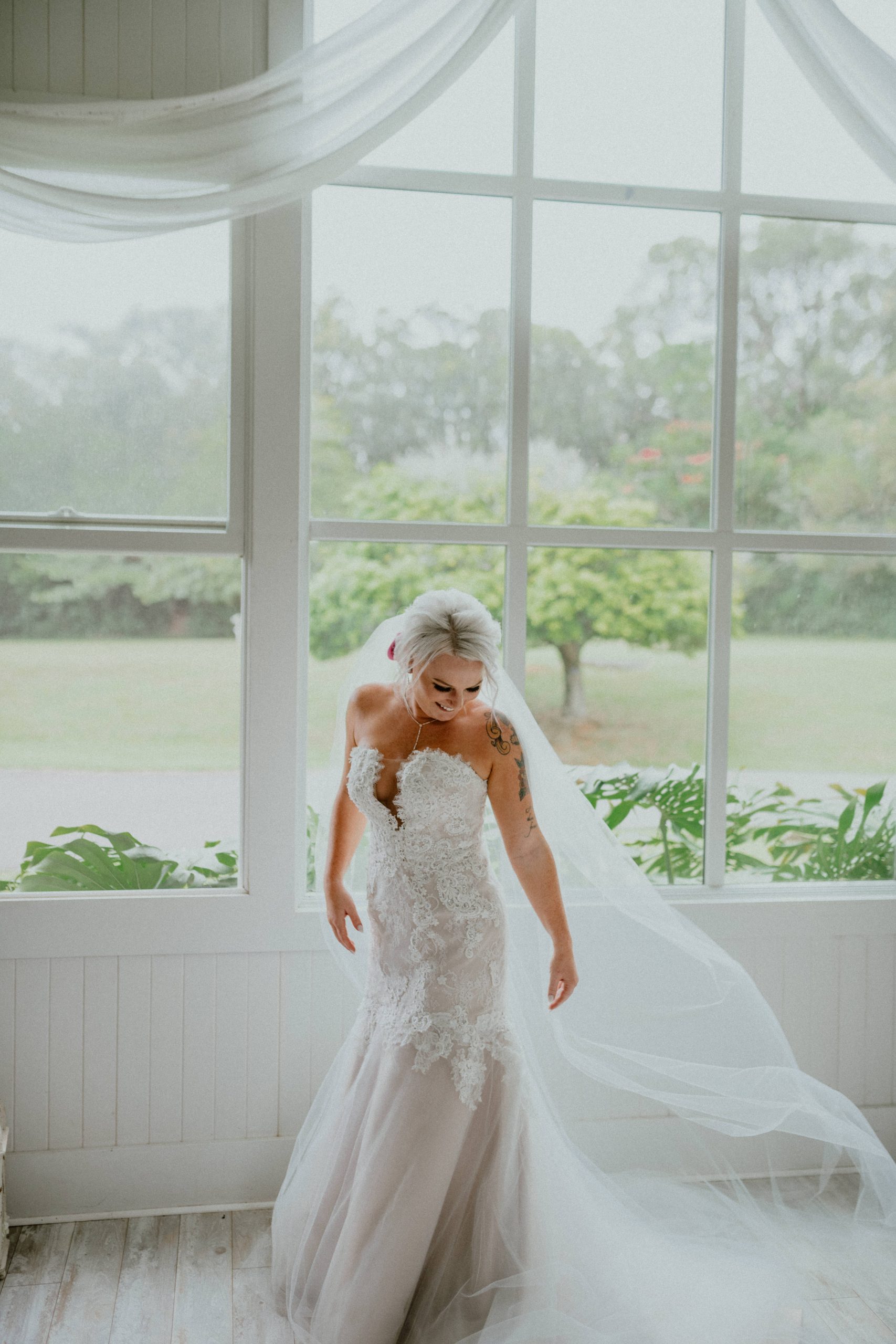 Bride in strapless wedding dress style and long tulle veil stands in front of a large window looking out at Hawaii scenery | Oahu Wedding Photographer, Oahu Elopement Photographer, Destination Wedding Photographer, Destination Elopement Photographer, Newlywed moments ideas, Newlywed Photography inspiration, Hawaii Elopement ideas | chelseaabril.com