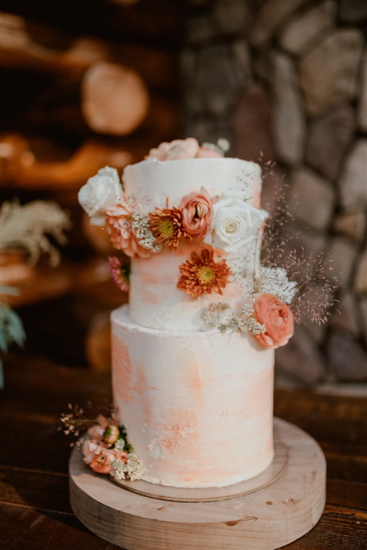 Fall inspired wedding cake of with orange and white fall florals added to the cake with boho wedding details on a wood table | Sun River Elopement, Destination Elopement Photographer, Smith Rock Elopement Inspiration, Oregon Elopement ideas, PNW Fall Wedding Inspiration, Fall Outdoor Wedding Ideas,Fall Wedding Inspiration, PNW Outdoor Wedding Ideas | chelseaabril.com
